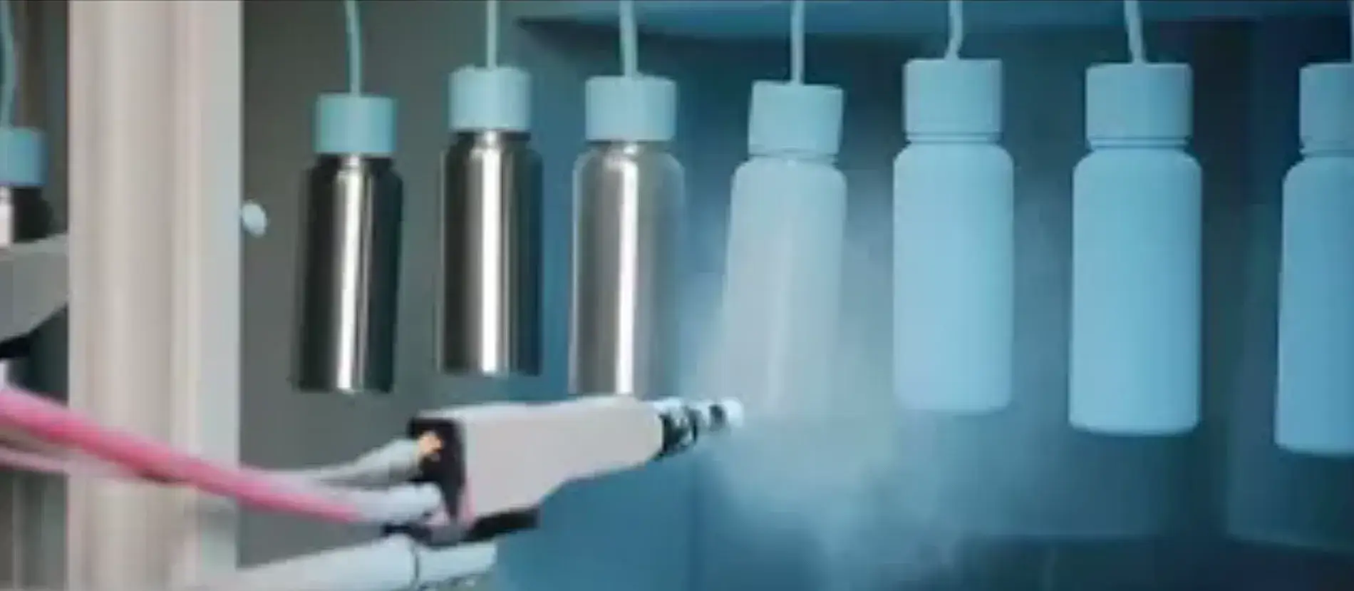Powder being electrostatically sprayed onto stainless steel bottle